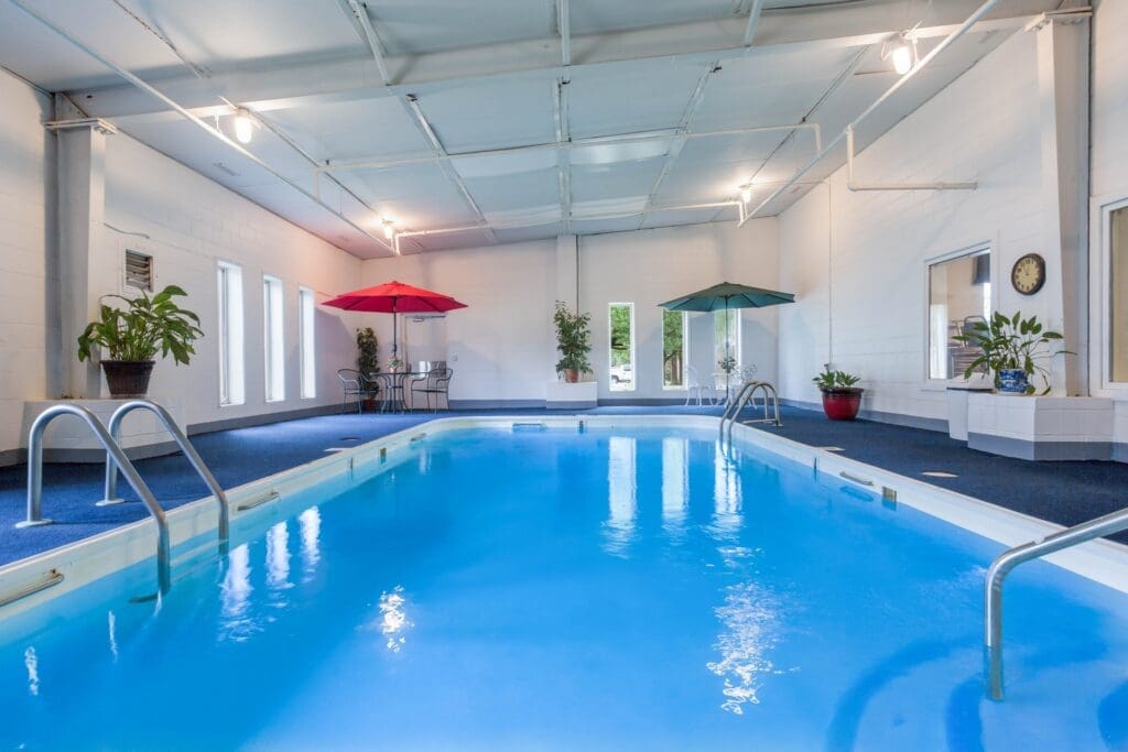 Indoor swimming pool with several tables and chairs in the lounge area and various plants